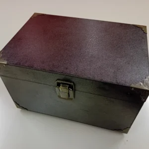 A closed black magician’s prop box with metallic vintage-style corner protectors and a latch lock, placed on a white surface.